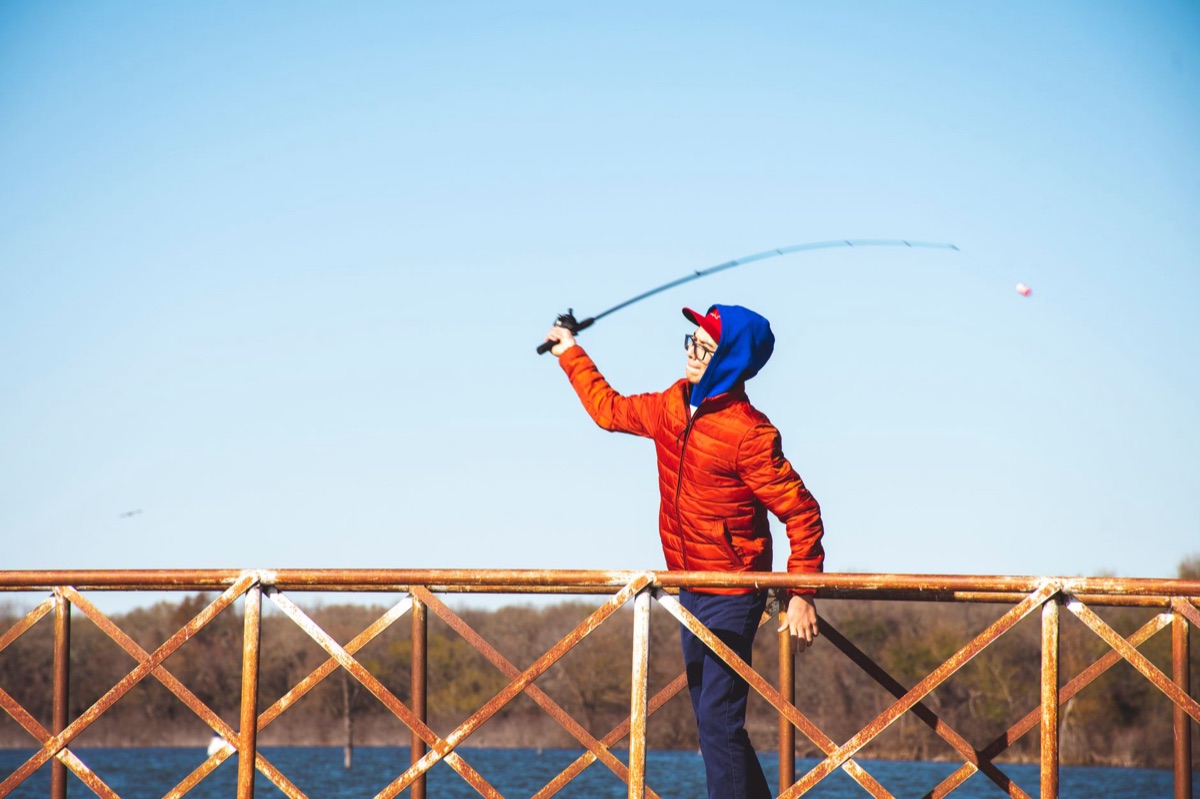 A fishing beginner casting a line from a boat, with the line in the air and the water reflecting the sunlight.