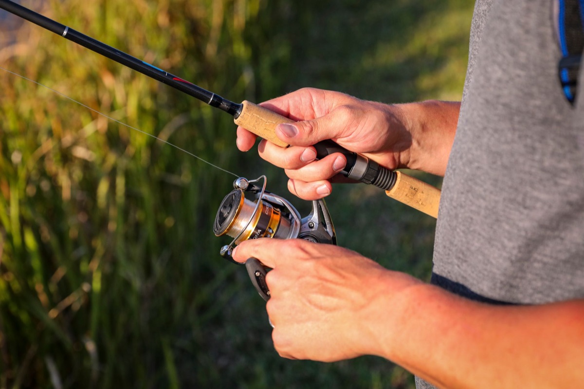 A fishing beginner holding a rod with a line in the air, casting from a boat with water reflecting the sunlight.