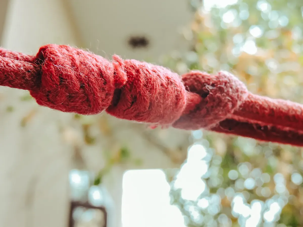 Detailed close-up of red rope with knots against a bokeh background, highlighting texture and focus.