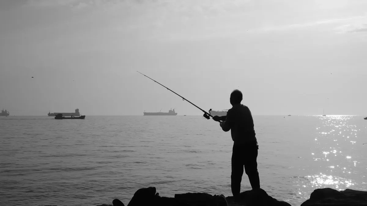 朝の光の中で海辺で静かなシーン。船が通り過ぎる中、男が漁っている。