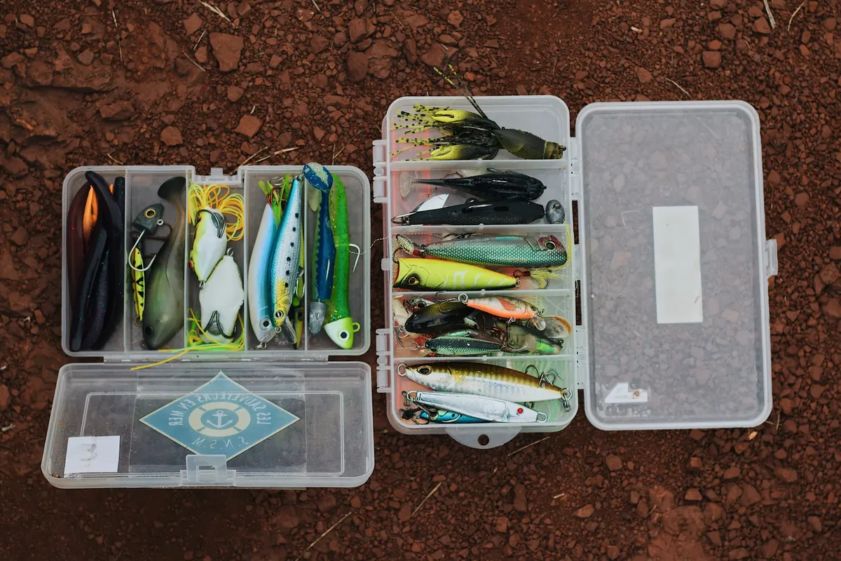 Open tackle boxes displaying colorful fishing lures on a rocky surface.