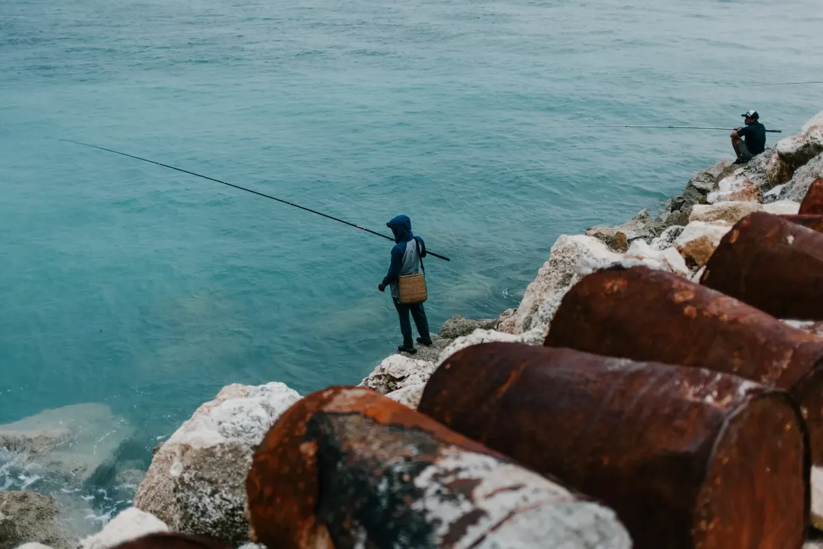 Two people fishing on a rocky shore by the sea, capturing tranquil coastal vibes.