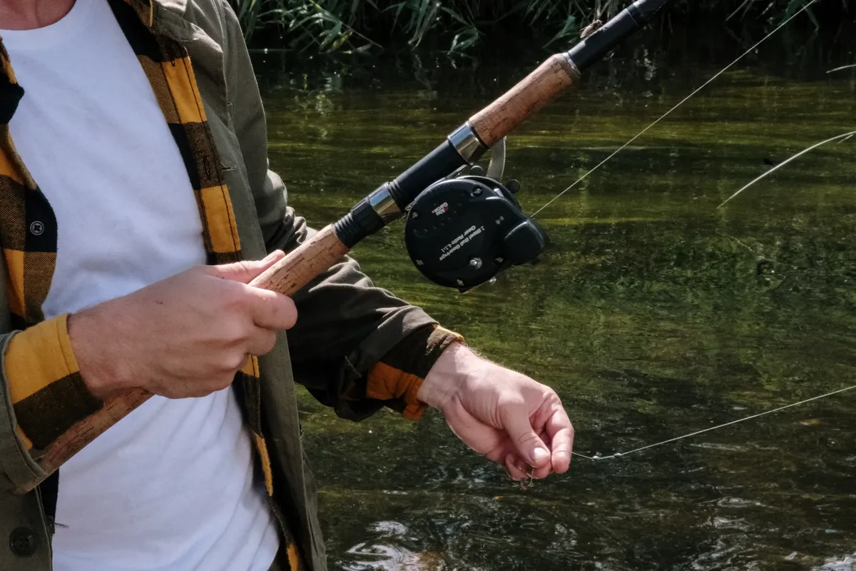 Close-up of a man fishing on a tranquil river, showcasing a fishing rod and reel.