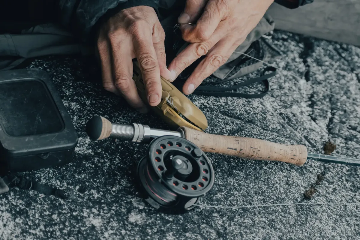 一張詳細展示 fishing gear 的照片，包含手在戶外岩石表面準備設備的場景。
