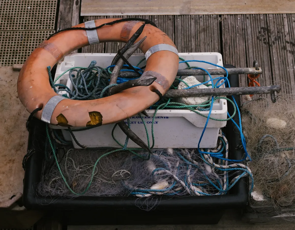 Close-up of marine equipment including fishing net, anchor, and lifebuoy on wooden deck.