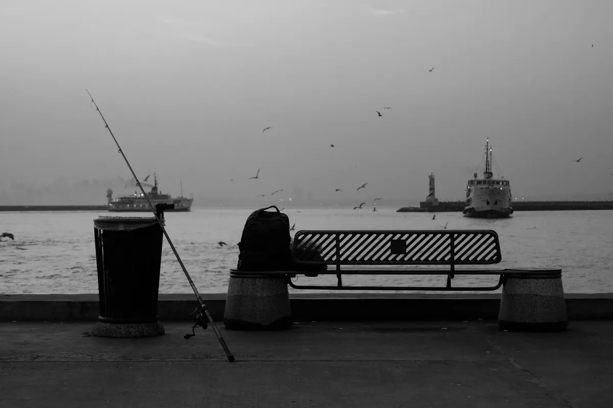Peaceful waterfront with a fishing rod, bench, and boats, capturing a tranquil moment.