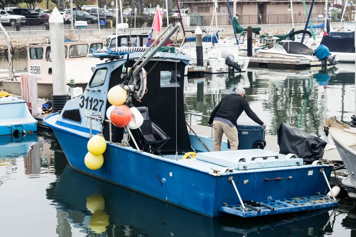 Fishing boat in a lively harbor with a man preparing equipment, surrounded by watercraft.